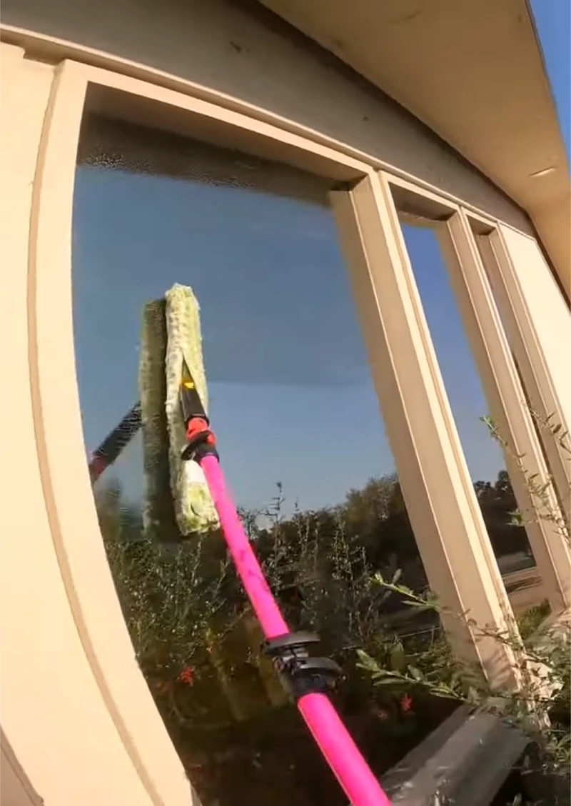 Water-fed pole brush cleaning a window with wood frames